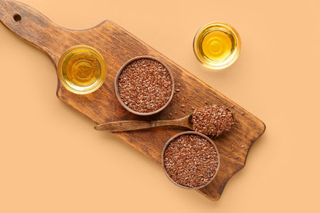 Wooden board with bowl of flax oil and seeds on orange backgroundの写真素材