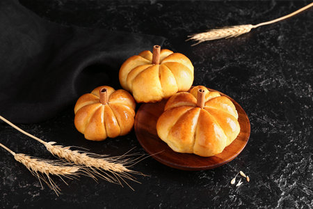 Plate with tasty pumpkin shaped buns on black background