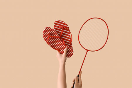 Female hands with flip flops and badminton racket on beige backgroundの写真素材
