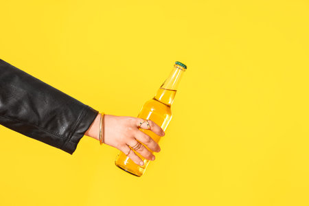 Female hand with bottle of cold tasty beer on yellow backgroundの写真素材