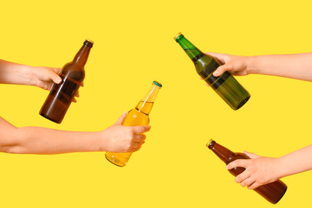 Female hands with bottles of cold beer on yellow backgroundの写真素材