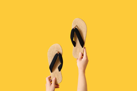 Female hands with flip flops on yellow backgroundの写真素材