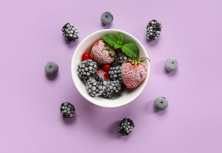 Bowl of frozen berries with mint leaves on purple background
