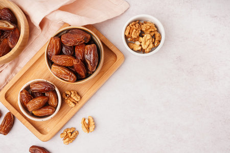 Bowls with dried dates and nuts on light background