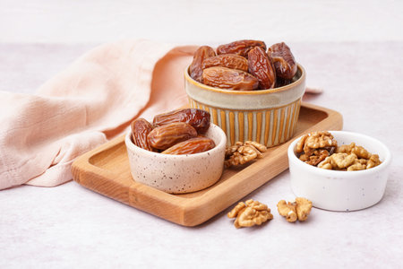 Bowls with dried dates and nuts on light background