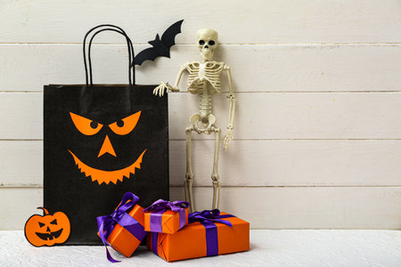 Composition with shopping bag, skeleton and gift boxes for Halloween on light wooden backgroundの写真素材