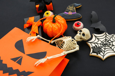 Composition with shopping bag, skeleton, gift boxes and tasty candies for Halloween on dark background, closeupの写真素材