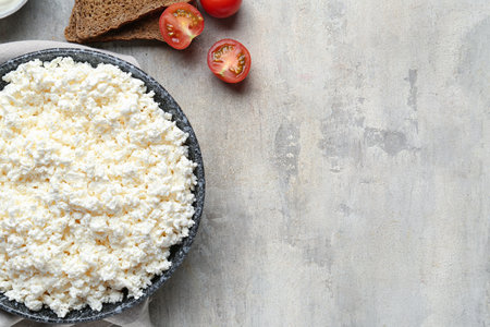 Fresh cottage cheese in bowl with bread pieces and tomatoes on gray tableの写真素材