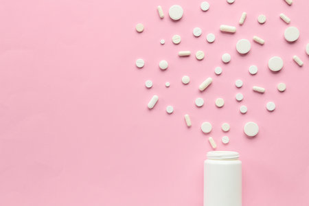 Different pills spilling out of pill bottle on pink backgroundの写真素材