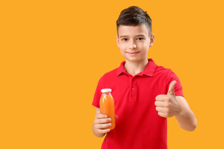 Little boy with bottle of orange juice showing thumb-up on color backgroundの写真素材