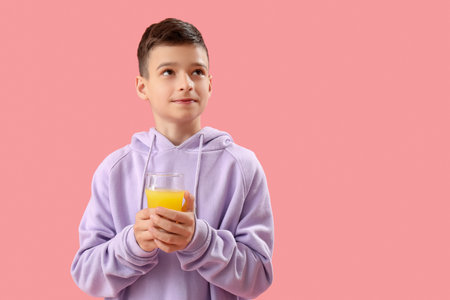 Little boy with glass of orange juice on pink backgroundの写真素材
