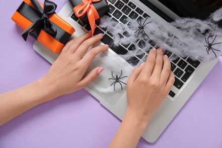 Female hands with modern laptop, gift boxes for Halloween on purple background, closeupの写真素材