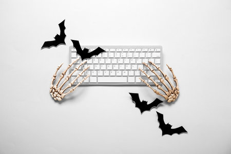 Composition with modern computer keyboard, skeleton hands and paper bats for Halloween on white backgroundの写真素材