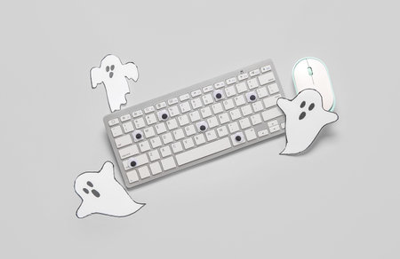 Composition with modern computer keyboard, mouse and paper ghosts for Halloween on gray background