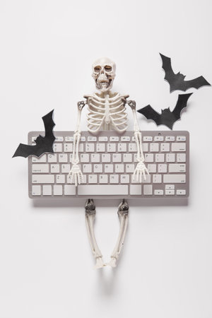 Composition with modern computer keyboard, skeleton and paper bats for Halloween on white backgroundの写真素材