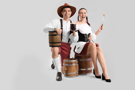 Young couple in traditional German clothes with beer and sausage on light backgroundの写真素材