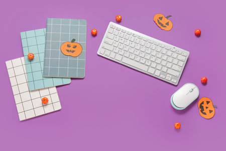 Composition with modern computer keyboard, mouse, notebooks and pumpkins for Halloween on purple...