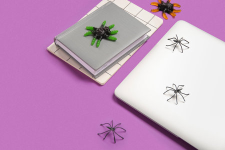 Modern laptop, notebooks and spiders for Halloween on purple background, closeup