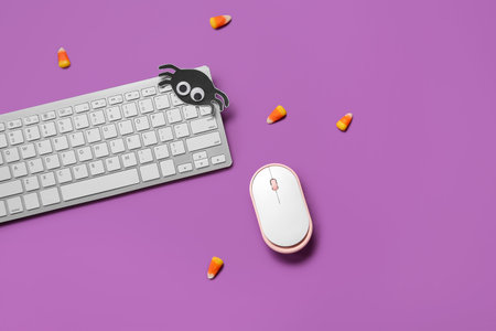 Composition with modern computer keyboard, mouse and tasty candy corns for Halloween on purple...