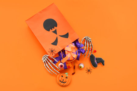 Composition with shopping bag, skeleton hands, gift boxes and tasty candies for Halloween on orange...