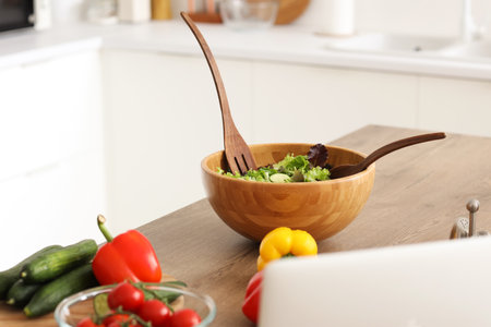 Wooden bowl with fresh salad on table in kitchen, closeupの写真素材