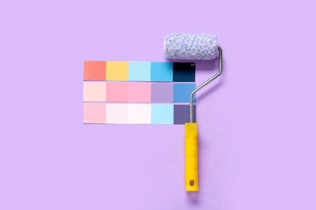 Many color palettes and paint rollers on lilac background, top view