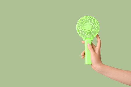 Hand of young woman with mini fan on green backgroundの写真素材