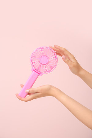 Hands of young woman with mini fan on pink backgroundの写真素材
