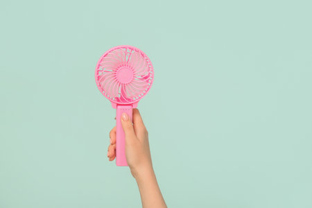Female hand with mini fan on blue backgroundの写真素材