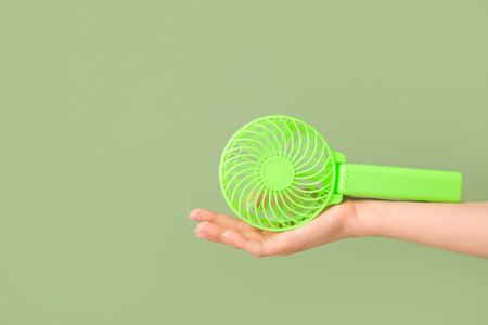 Hand of young woman with mini fan on green backgroundの写真素材