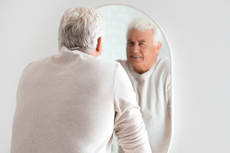Senior man looking in mirror at homeの写真素材