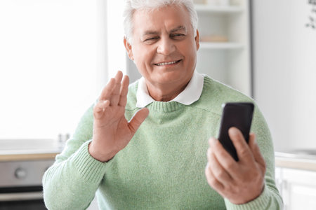 senior man with mobile phone video chatting in kitchen