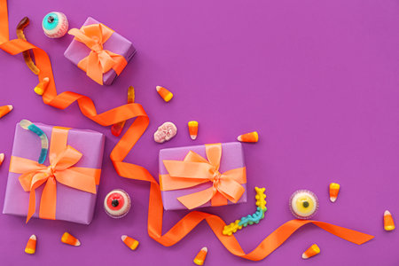 Composition with gift boxes and tasty candies for Halloween on purple backgroundの写真素材