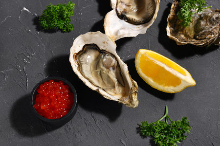 Tasty oysters with lemon and red caviar on black background