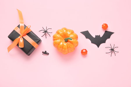 Composition with gift box, pumpkins, paper bat and spiders on pink background. halloween celebration conceptの写真素材