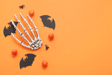 Composition with pumpkins, skeleton hand, paper bats and spiders on orange background. halloween celebration conceptの写真素材