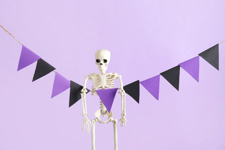 Garland made of paper flags and skeleton for Halloween celebration on purple backgroundの写真素材