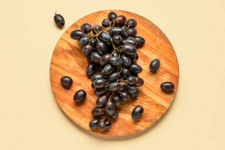 Wooden board with sweet black grapes on yellow backgroundの写真素材