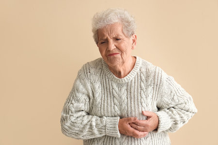 Elderly woman having heart attack on beige backgroundの写真素材