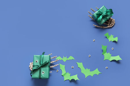 Composition with beautiful gift boxes, skeleton hands and Halloween decor on blue backgroundの写真素材
