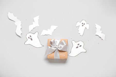 Composition with beautiful gift box, ghosts and bats made of paper for Halloween on light backgroundの写真素材