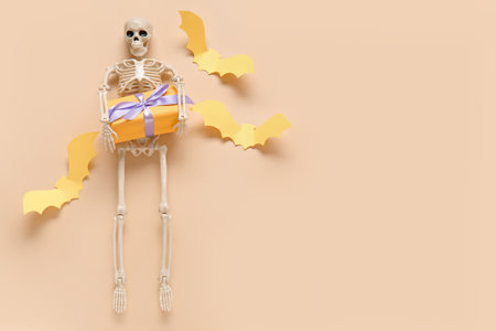 Composition with skeleton, beautiful gift box and bats made of paper for Halloween on beige backgroundの写真素材