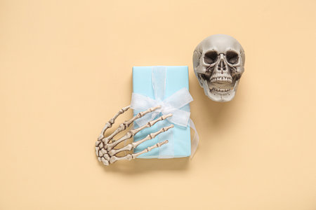 Composition with beautiful gift box, skeleton hand and skull for Halloween on beige backgroundの写真素材