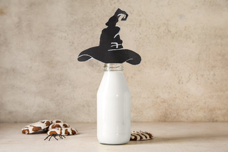 Bottle of milk, tasty cookies and hat made of paper for Halloween on light backgroundの写真素材