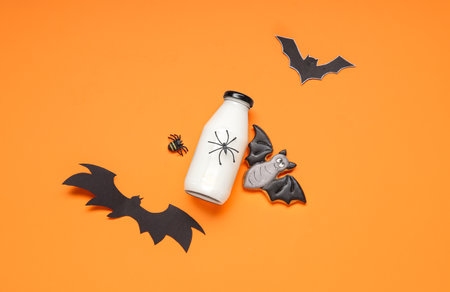 Bottle of milk, bats made of paper and tasty cookie for Halloween on orange backgroundの写真素材