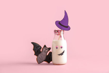 Bottle of milk, tasty cookie and hat made of paper for Halloween on pink backgroundの写真素材