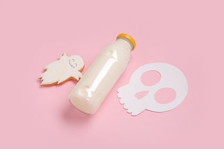 Bottle of milk and skull made of paper and tasty cookie for Halloween on pink backgroundの写真素材