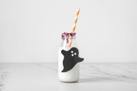 Bottle of milk, ghost made of paper and sprinkles for Halloween on light backgroundの写真素材