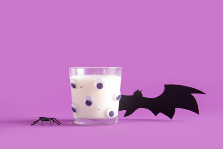 Glass of milk and bat made of paper for Halloween on purple background, closeupの写真素材