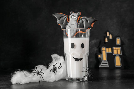 Glass of milk, spiders and tasty cookie for Halloween on dark background, closeupの写真素材